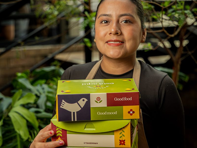 Una colaboradora de Tagers sonríe con una pila de cajas de Box Lunch cerradas