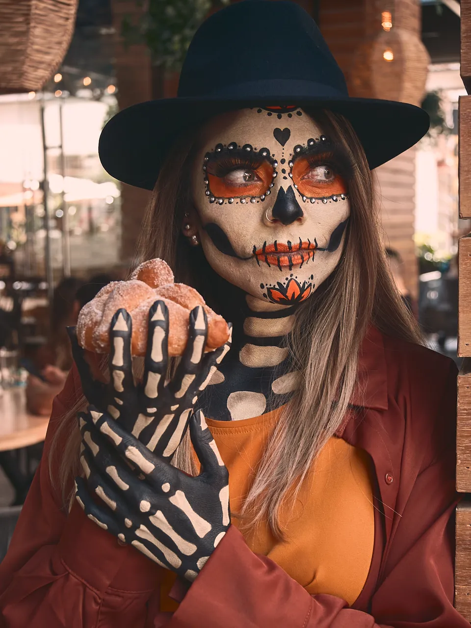 La catrina, de maquillaje blanco y naranja, sostiene un pan de muerto con su guante de esqueleto
