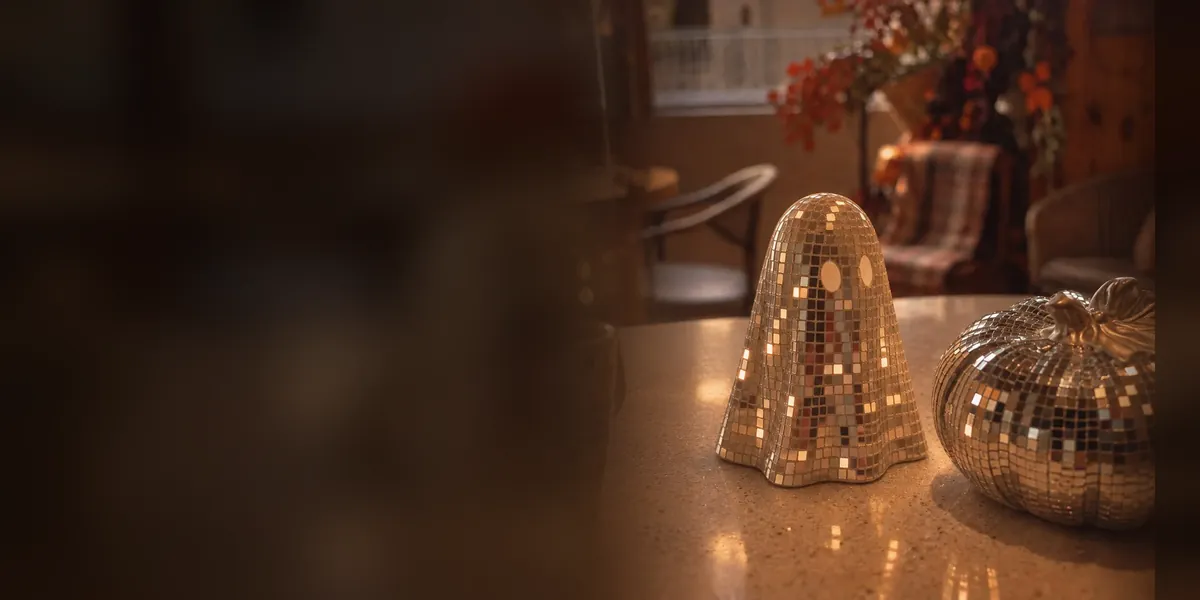 Un fantasma y una calabaza cubiertos de espejitos dorados brillan sobre una mesa con luz cálida de otoño
