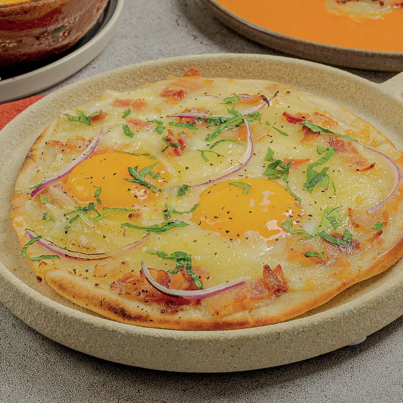 Brunch flatbread with two fried eggs, bacon and melted manchego cheese