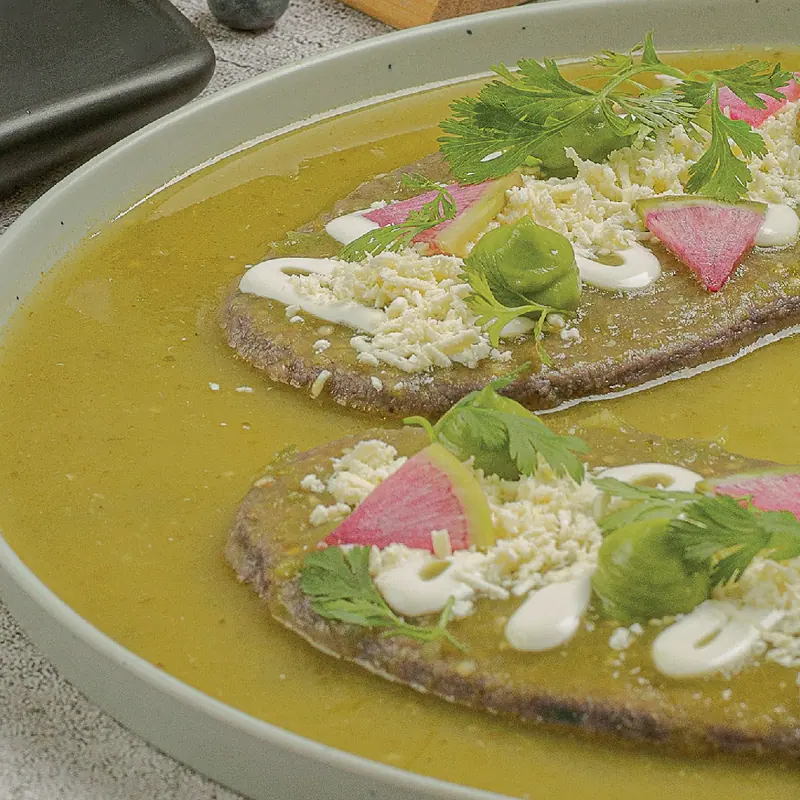 Tlacoyos drowned in green salsa with cream, cheese and radish