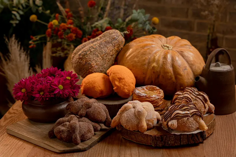 Pan de muerto, conchas de calabaza y pays de temporada sobre una mesa con calabazas