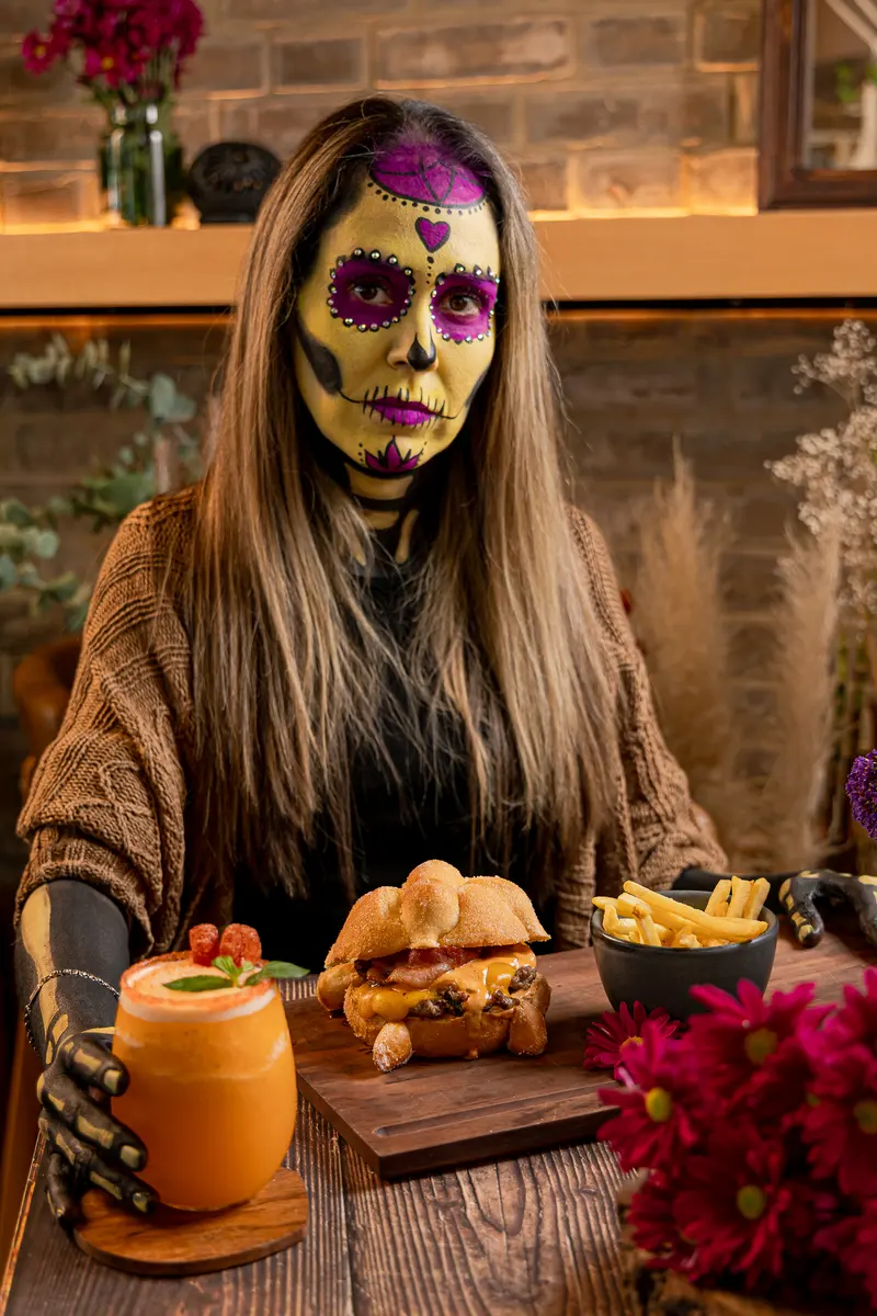 Una catrina de rostro pintado sentada a la mesa con la Catrina smash burger
