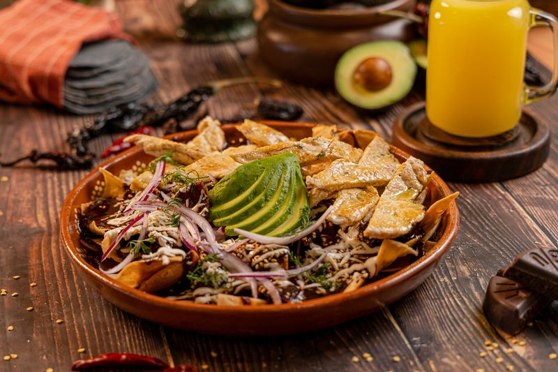 Chilakillers: totopos bañados en mole poblano con pollo, aguacate, crema y cebolla morada