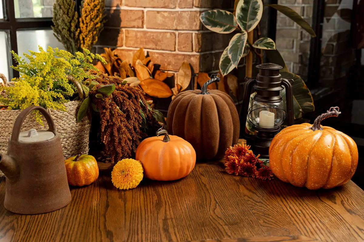 Mesa de madera con calabazas, flores de cempasúchil y una lámpara de aceite