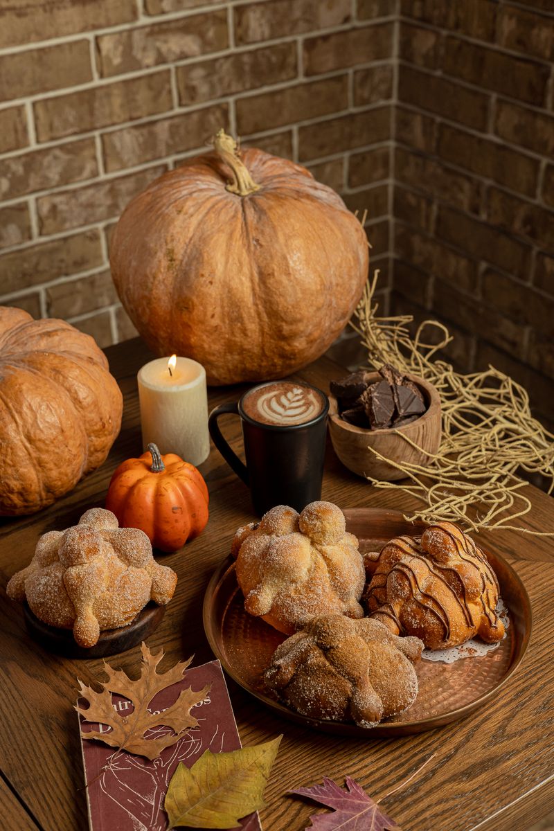 Pan de muerto de la casa con una vela encendida, un latte y una calabaza al fondo
