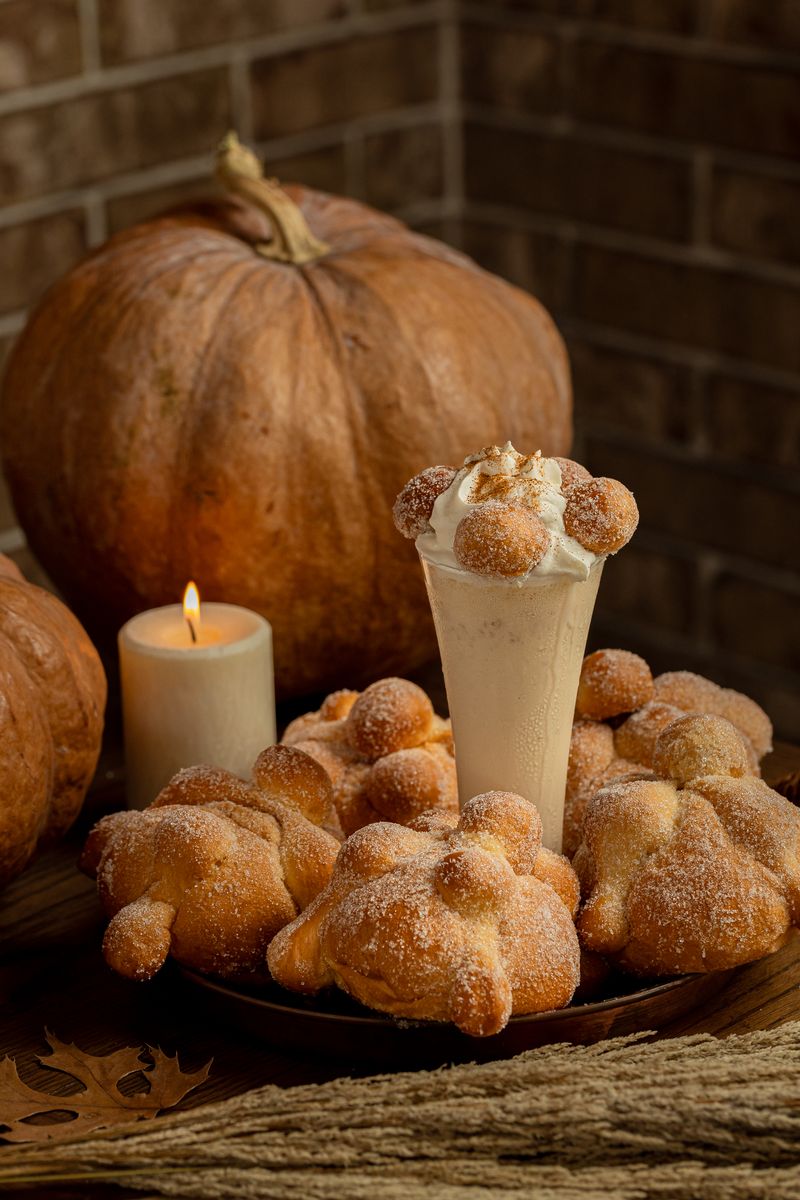 Pan de muerto y una vela encendida frente a una calabaza de Castilla, junto a una malteada de pan de muerto