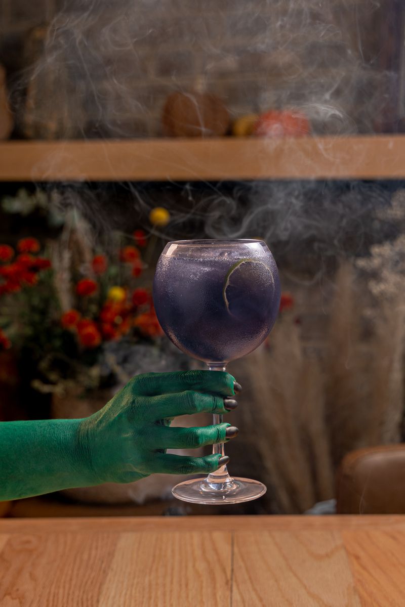 Pócima de brujas: una mano verde de bruja sostiene la copa morada entre humo