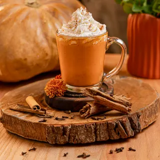 Pumpkin chai caliente con crema batida y canela frente a una calabaza