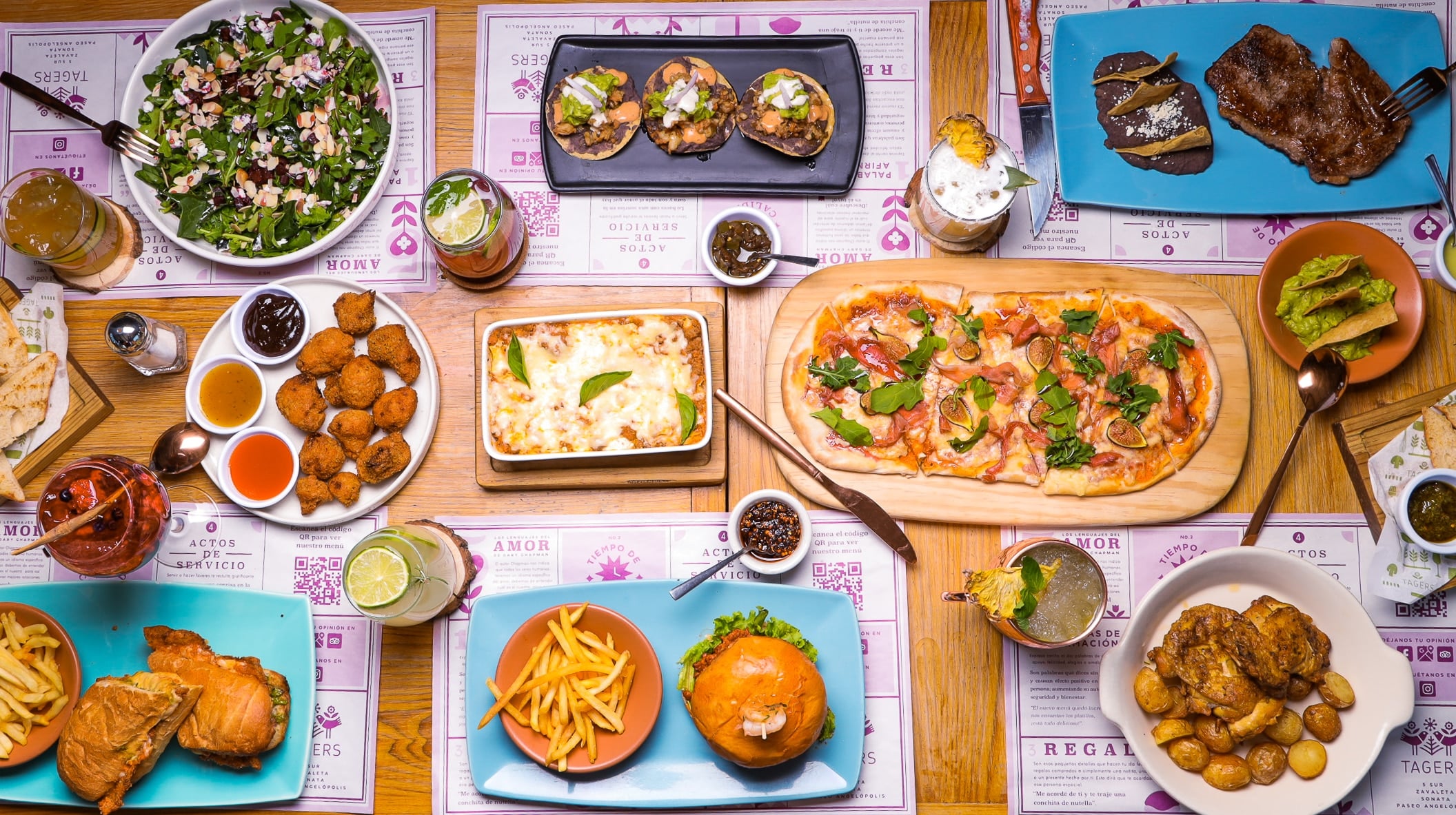 Mesa de comida en Tagers: flatbread, ensalada, tostadas de atún, burger y coctelería