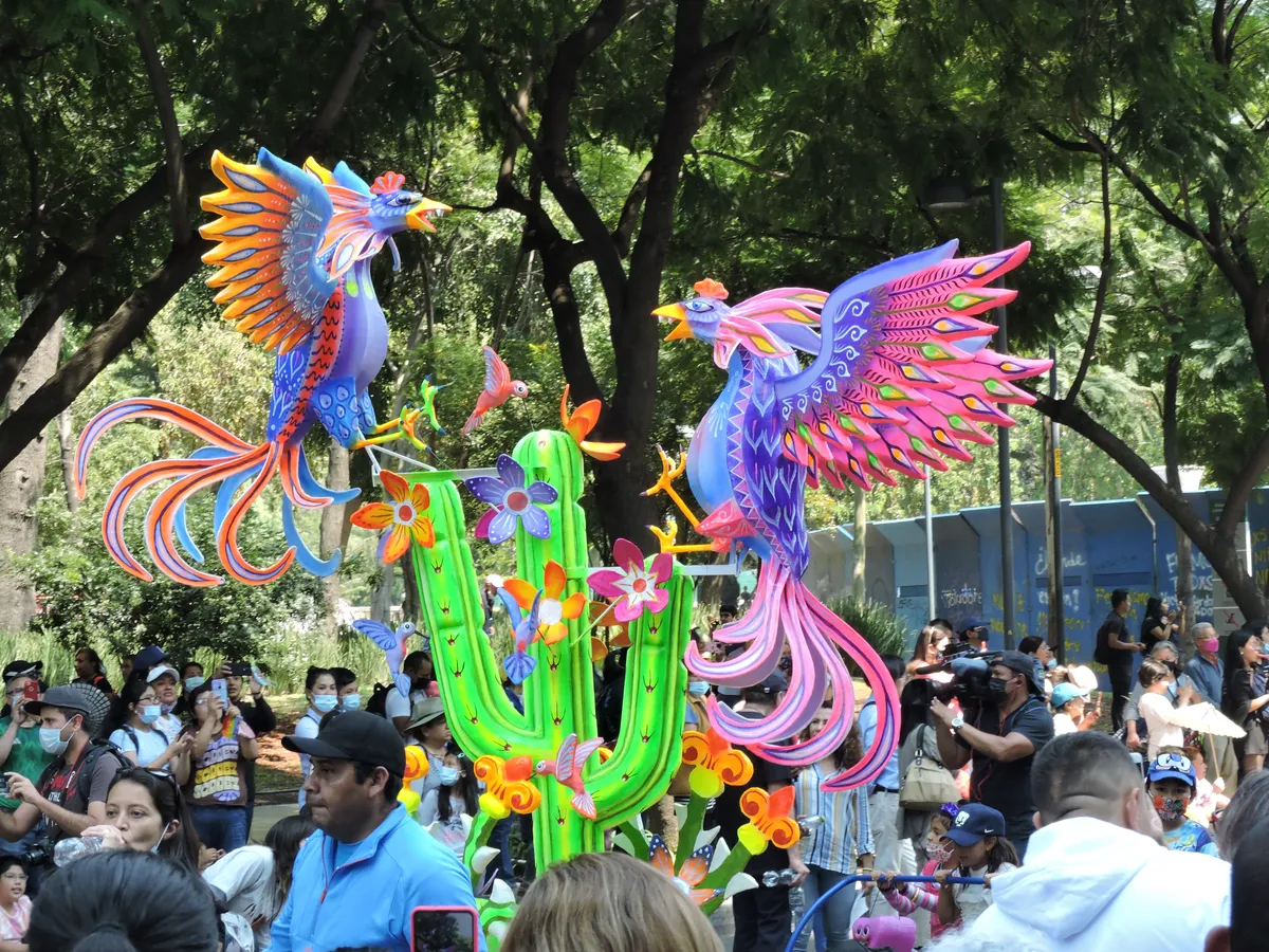 Alebrije monumental de dos gallos de colores junto a un cactus, rodeado de público en el desfile de alebrijes de la Ciudad de México