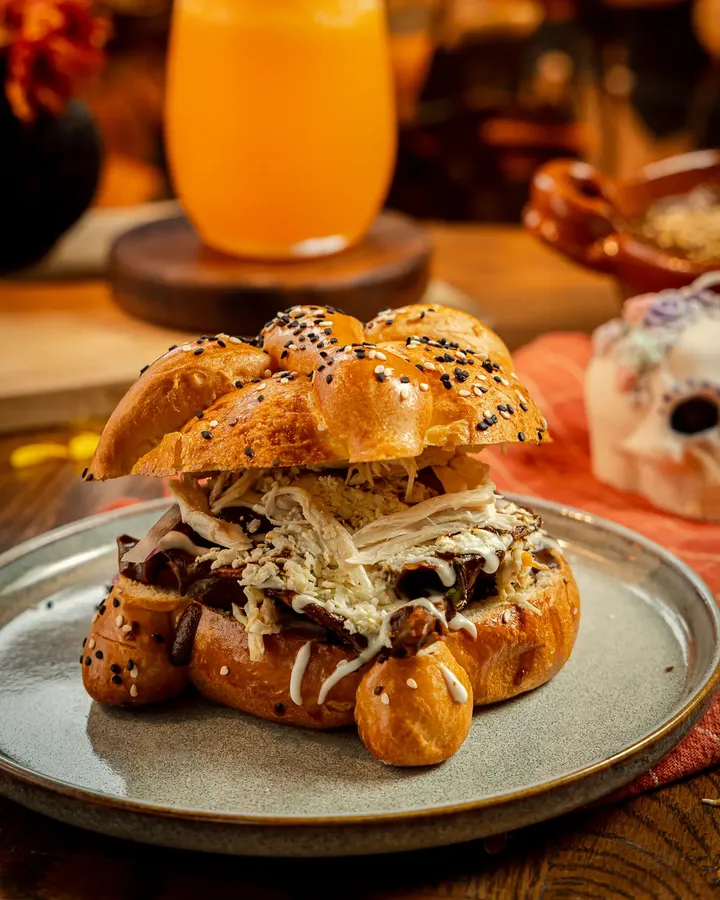 Catrin de mole de Tagers: pan de muerto de ajonjolí relleno de chilaquiles en salsa de mole, pollo deshebrado, queso y crema