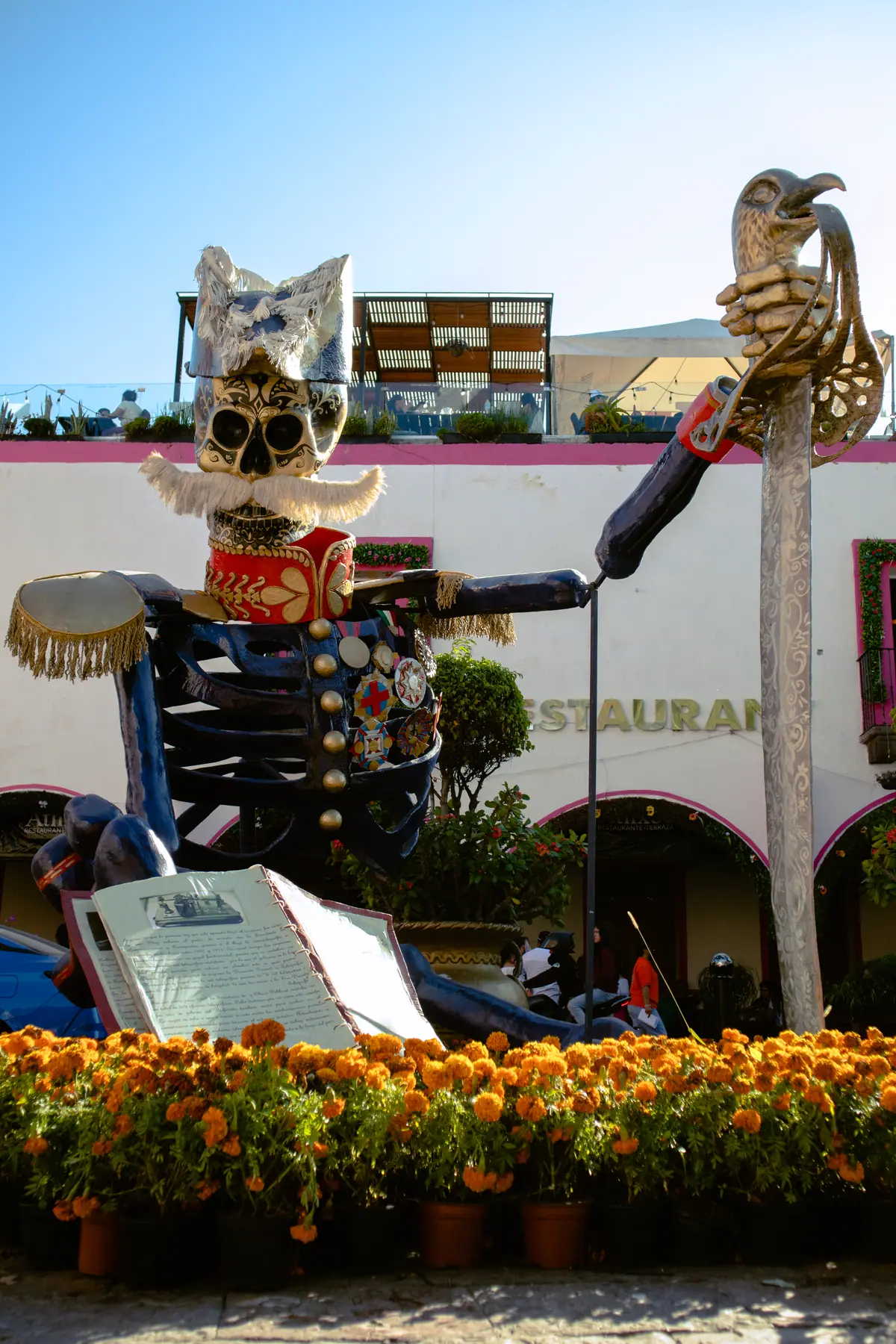 Catrina monumental de Porfirio Díaz junto a una fachada rosa, con flores de cempasúchil al frente, en Atlixco en 2024