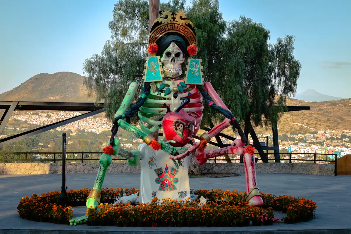 Catrina monumental de La Malinche sentada, con flores de cempasúchil alrededor y los cerros de Atlixco al fondo, en el Valle de Catrinas de 2024