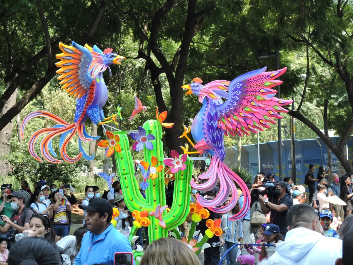 Alebrije monumental de dos gallos de colores junto a un cactus, rodeado de público en el desfile de alebrijes de la Ciudad de México