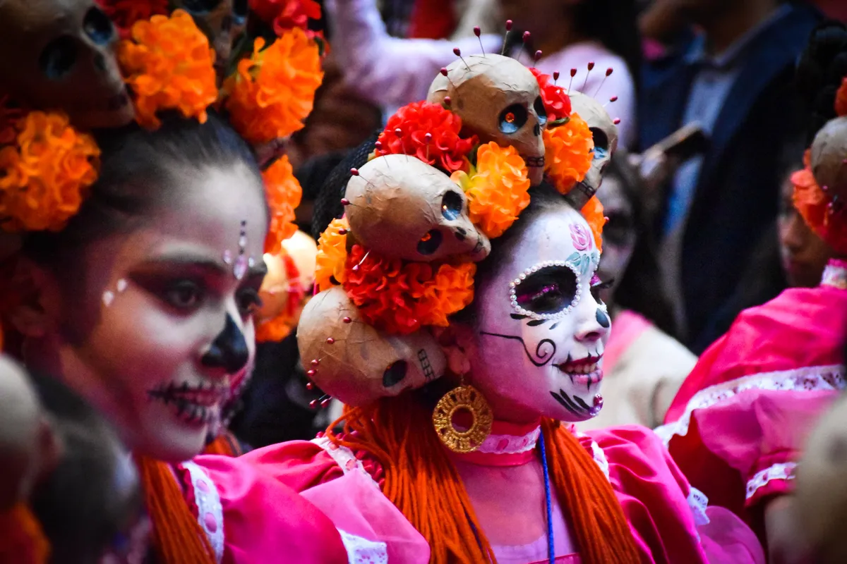 Dos mujeres con el rostro pintado de catrina y coronas de flores de cempasúchil en la Mega Procesión de Catrinas de la Ciudad de México