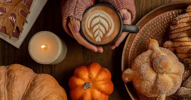 Pan de muerto azucarado junto a un café con leche en una mesa de otoño
