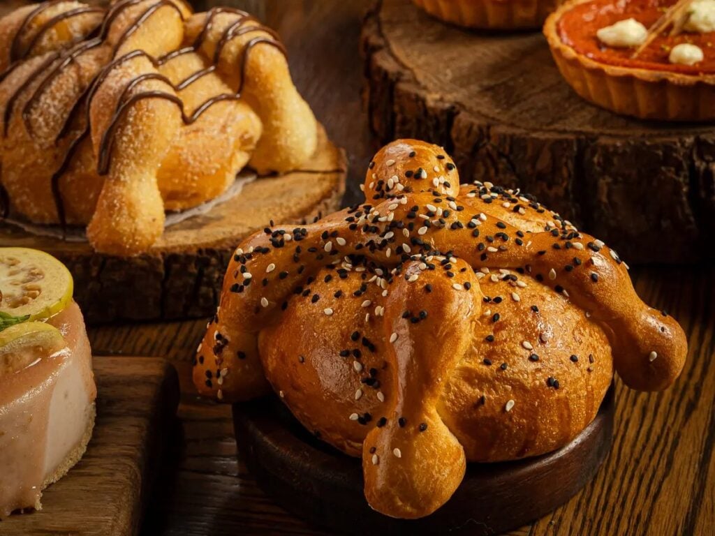 Pan de muerto con ajonjolí de Tagers, junto a pan de muerto de chocolate y pay de calabaza