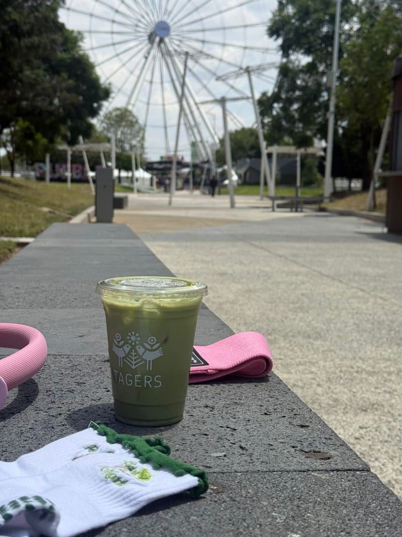 Andador del Parque Sendela con árboles, bancas y la Estrella de Puebla al fondo; en primer plano, un matcha de Tagers