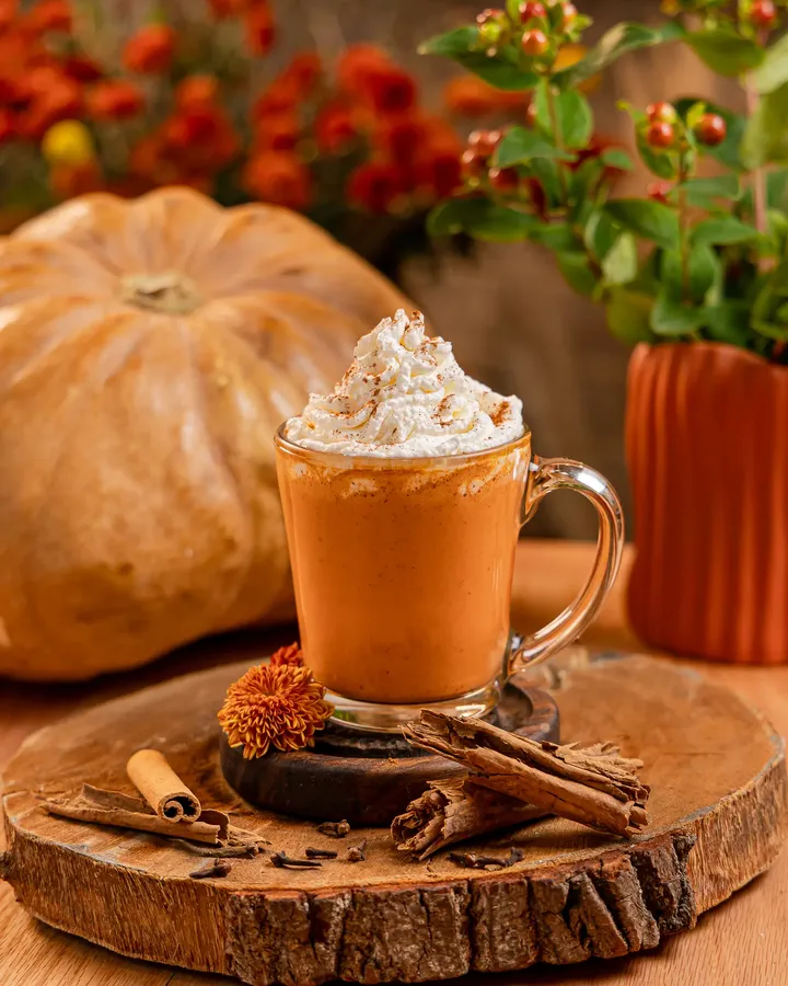 Pumpkin chai de Tagers en taza de vidrio con crema batida, rodeado de canela y calabazas