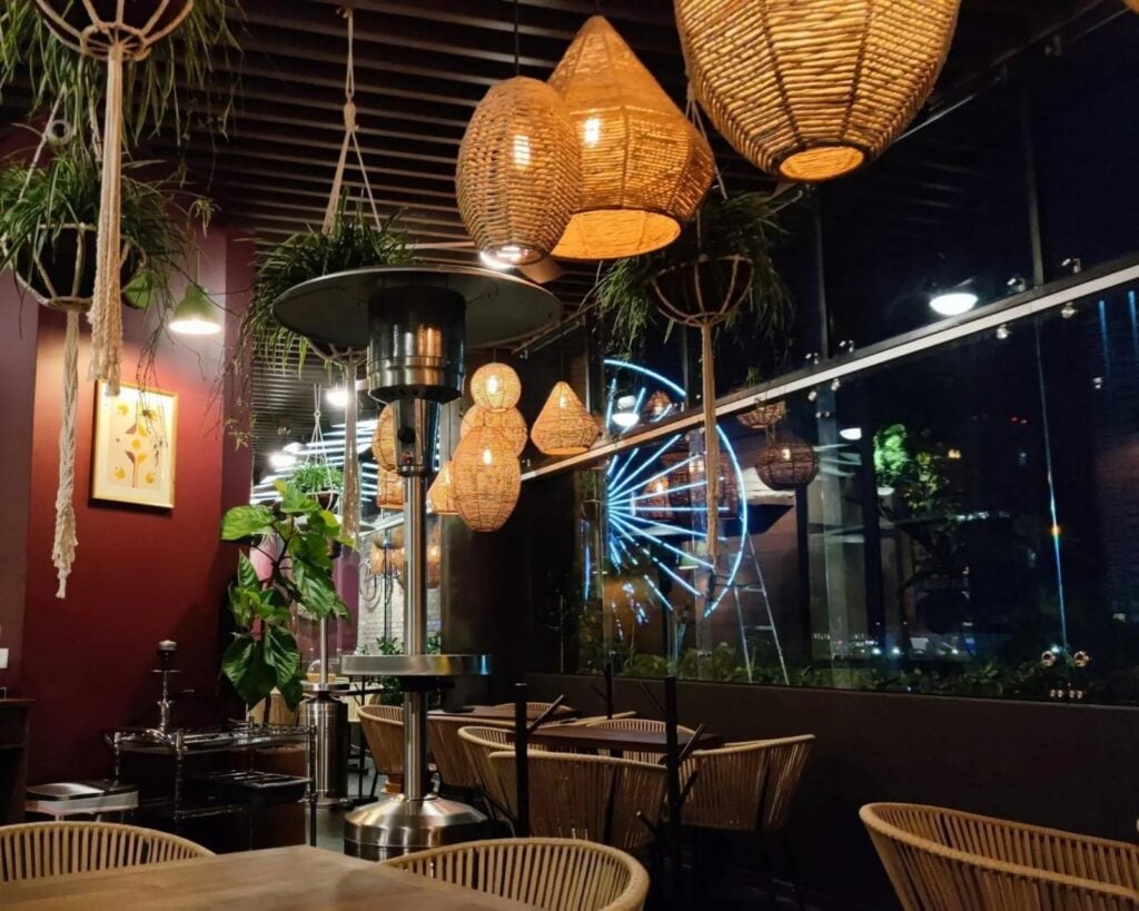 Terraza de Tagers Paseo Angelópolis de noche, con la Estrella de Puebla iluminada detrás del cristal