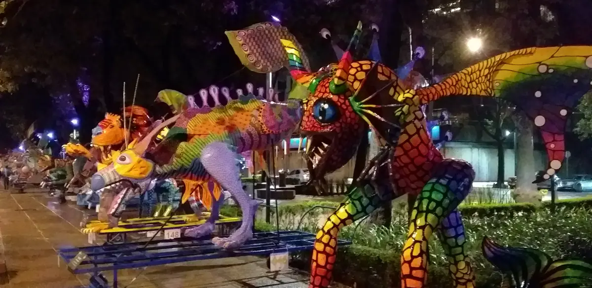 Hilera de alebrijes monumentales sobre plataformas a lo largo de Paseo de la Reforma, de noche, con las luces de la calle