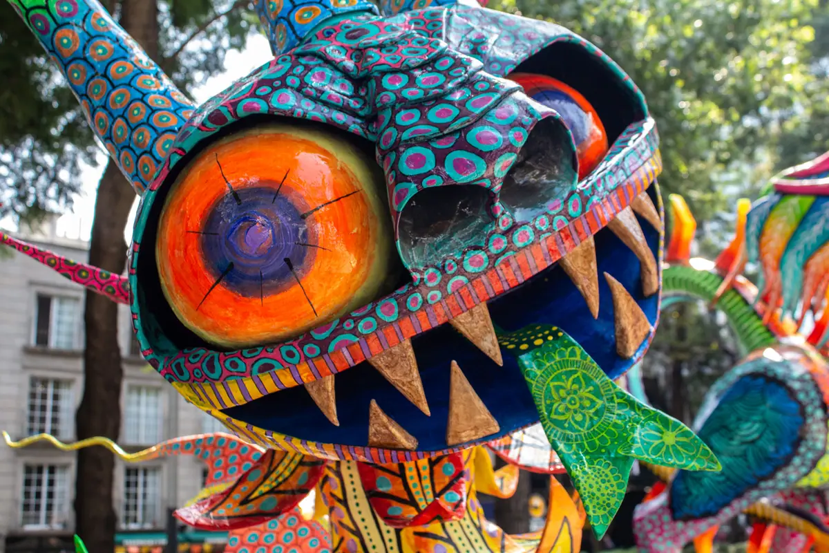 La cabeza de un alebrije monumental exhibido en Paseo de la Reforma, con edificios y la avenida detrás
