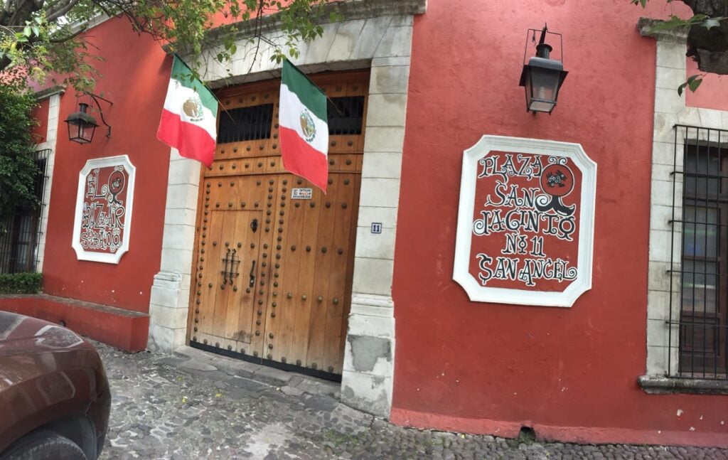 La fachada roja del Bazar del Sábado en Plaza San Jacinto 11, con su puerta de madera y dos banderas