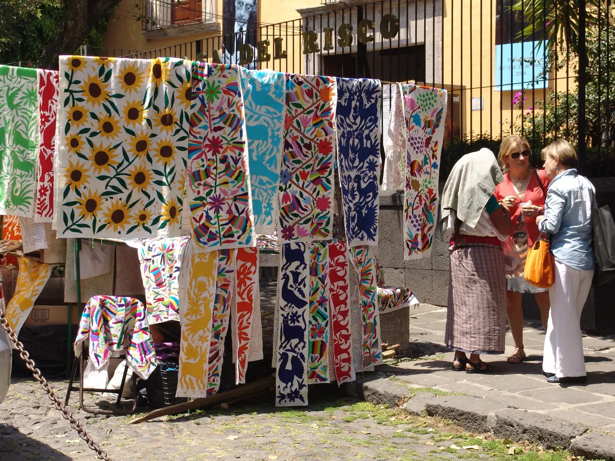 Bordados otomíes con girasoles y animales de colores colgados frente a la reja de la Casa del Risco