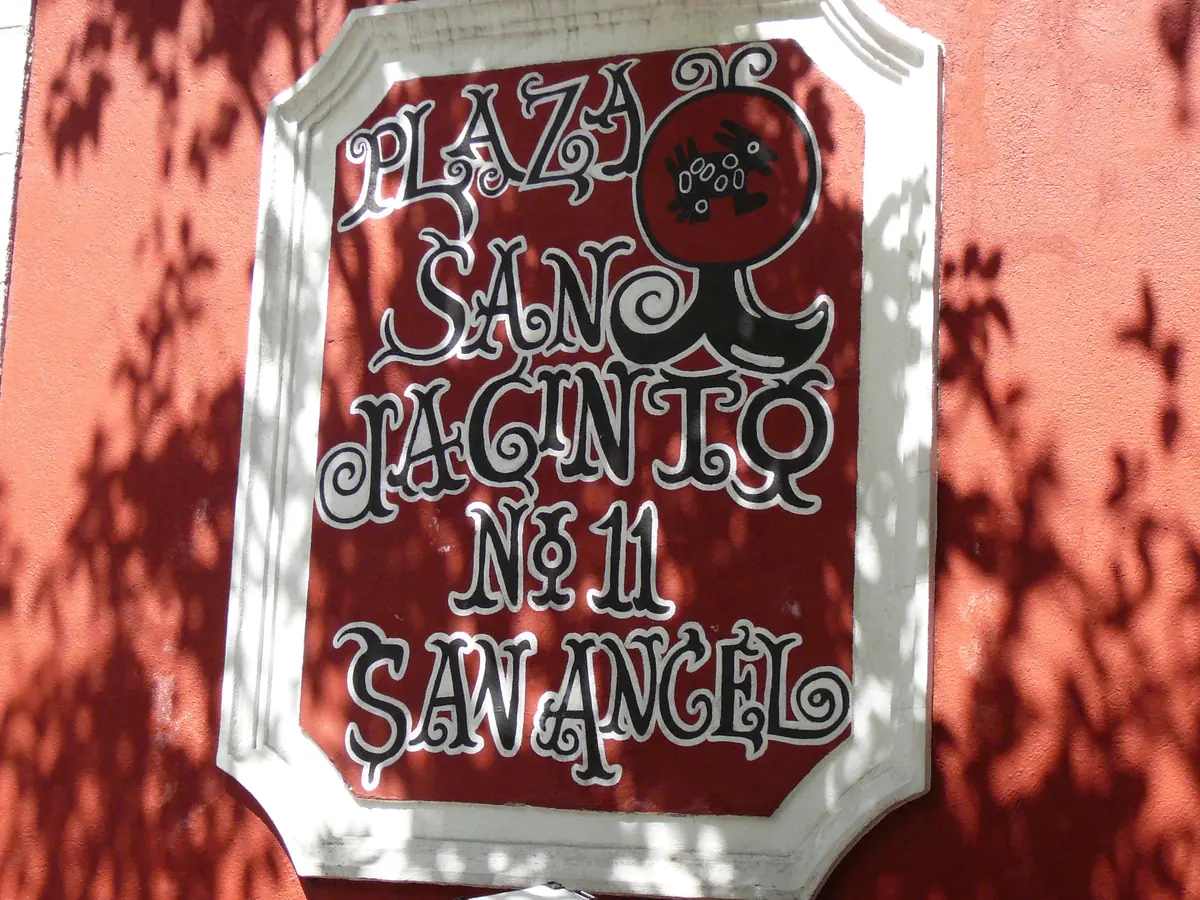 El letrero pintado «Plaza San Jacinto No. 11 San Ángel» en la pared roja del Bazar del Sábado