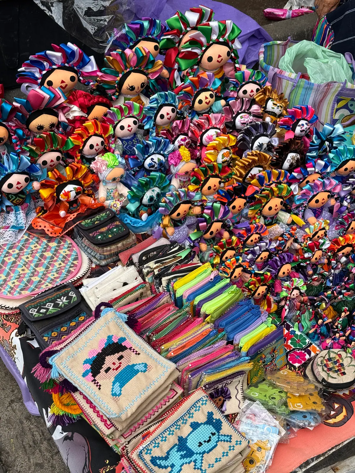 Muñecas de trapo con listones de colores y monederos bordados con figuras de muñecas, a la venta en un puesto del Jardín Centenario