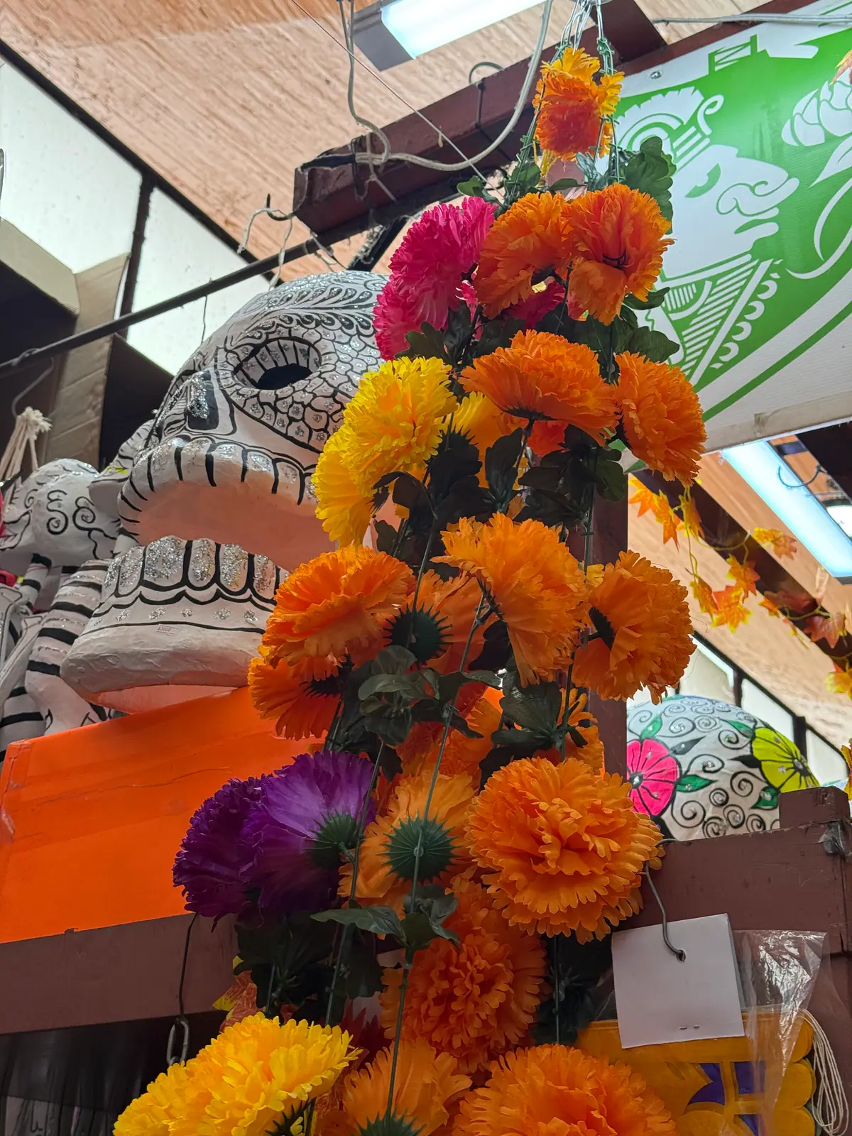 Una calavera grande pintada de blanco y negro entre una guirnalda de flores de cempasúchil naranjas y amarillas, en un puesto del Mercado de Coyoacán