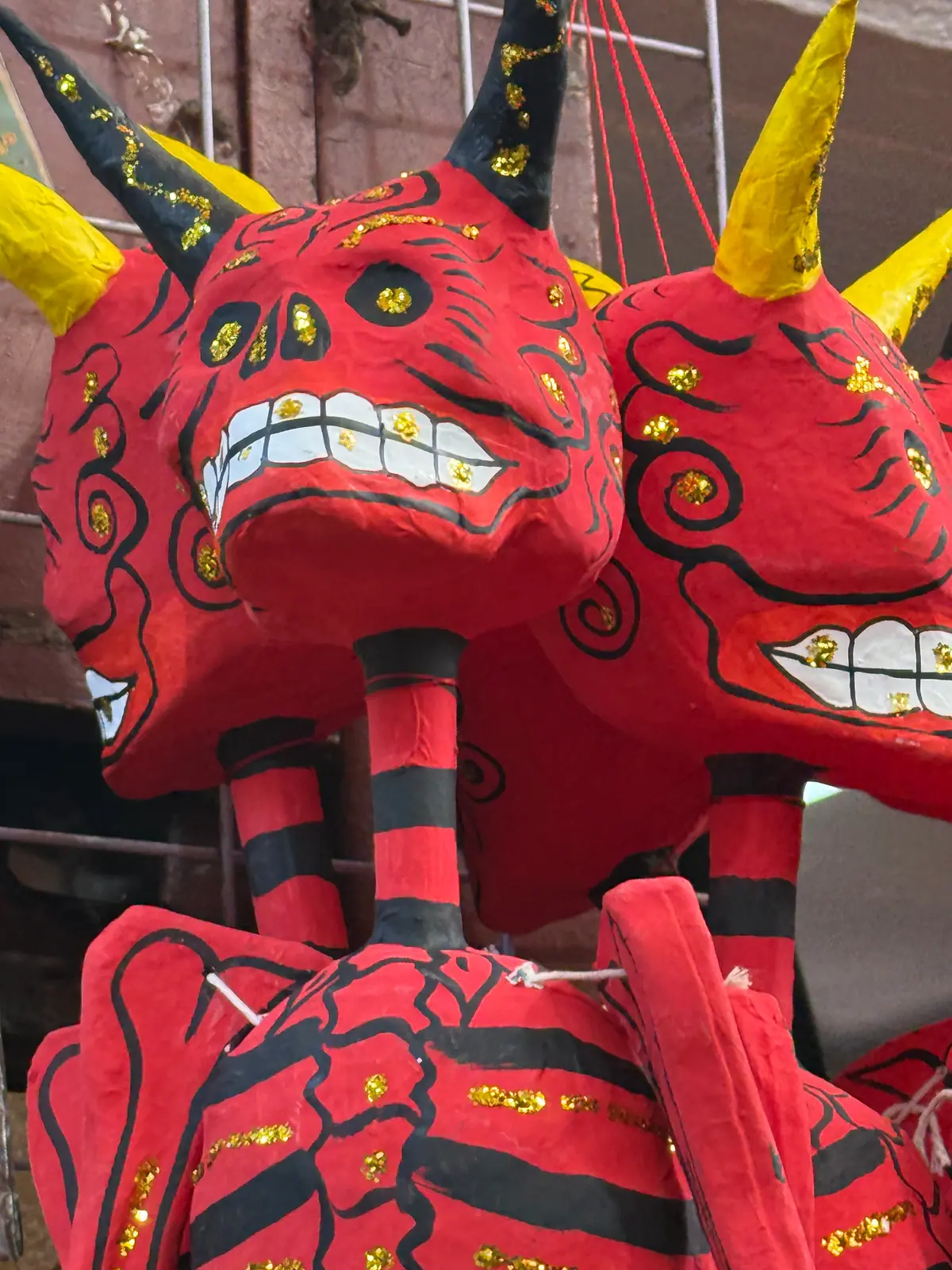 Diablos de cartón rojos con cuernos amarillos y negros, calavera sonriente y huesos pintados de negro, colgados del techo