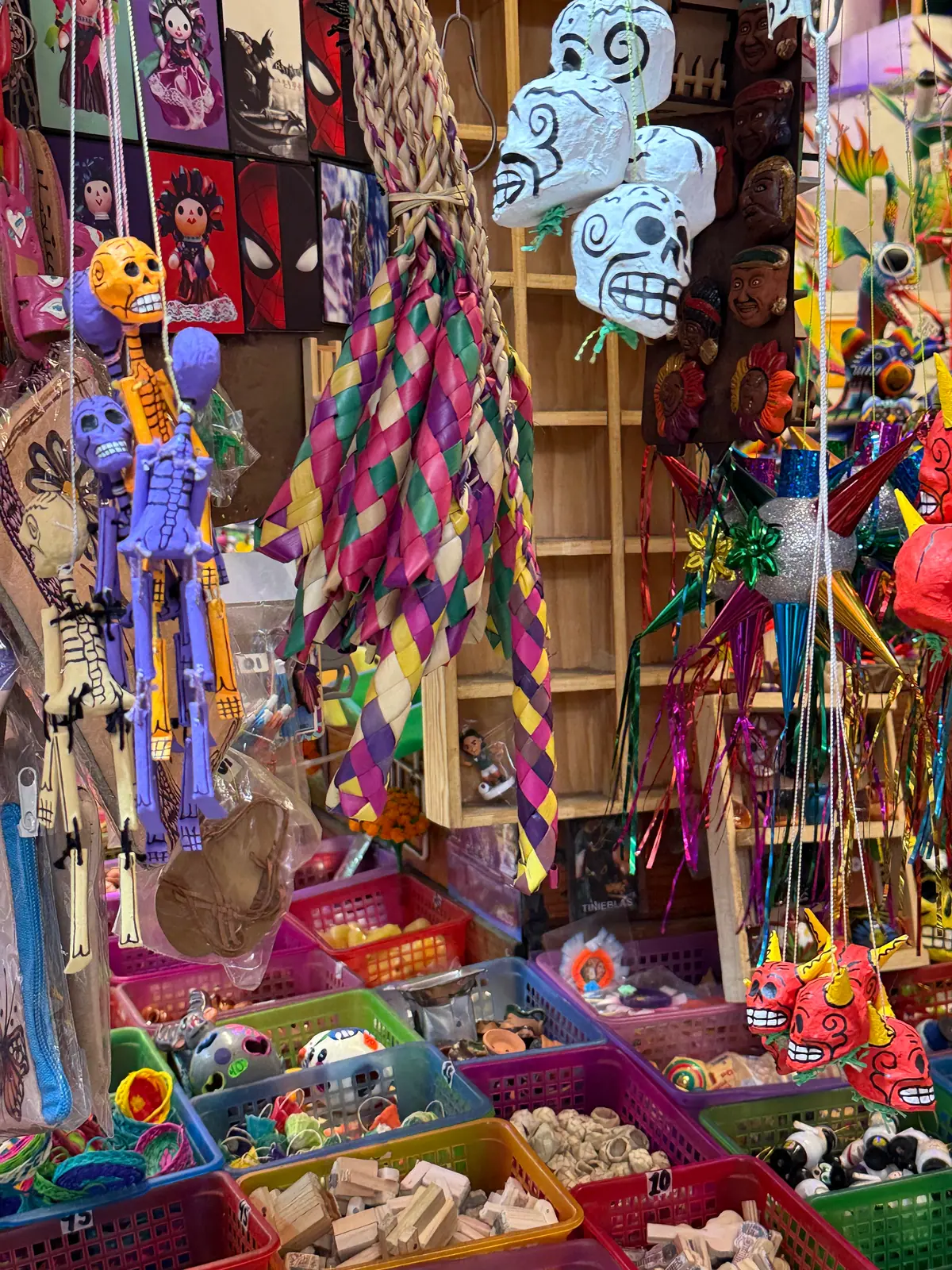 Un puesto con esqueletos de juguete colgados, calaveras de cartón blancas, piñatas de picos y canastas con juguetes de madera