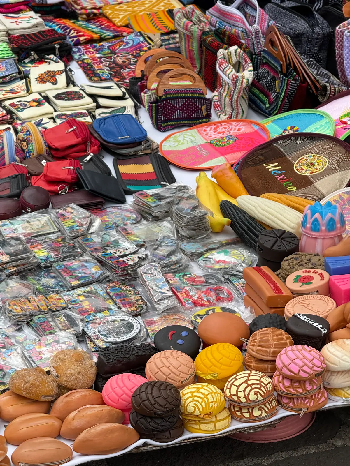Monederos con forma de conchas y bolillos, junto a otros con forma de dulces mexicanos, imanes y bolsas tejidas, en un puesto del Jardín Centenario de Coyoacán