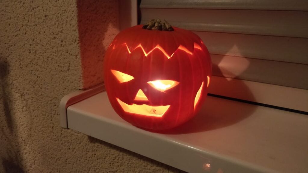 Una calabaza tallada de Halloween con la vela encendida adentro, sobre el marco de una ventana de noche