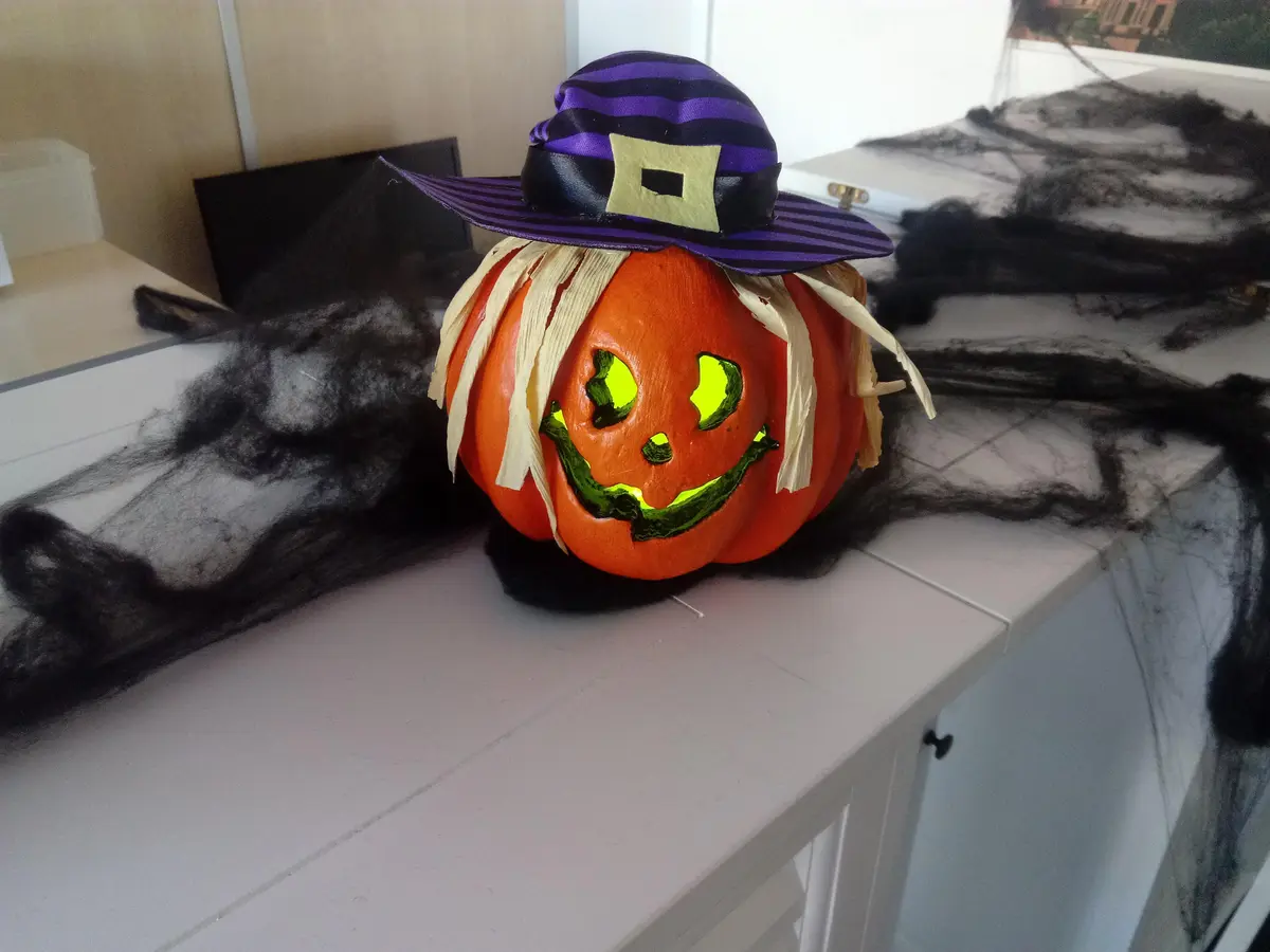 Una calabaza pequeña con sombrero de bruja y cara verde iluminada, sobre una barra de cocina
