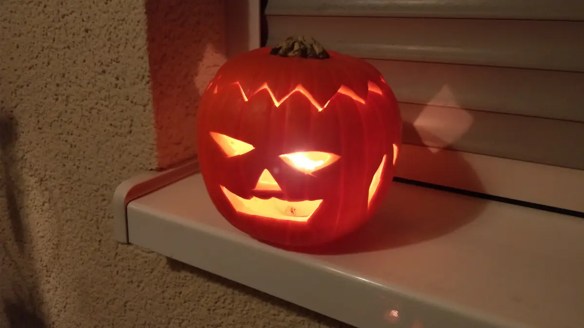 Una calabaza tallada de Halloween con la vela encendida adentro, sobre el marco de una ventana de noche