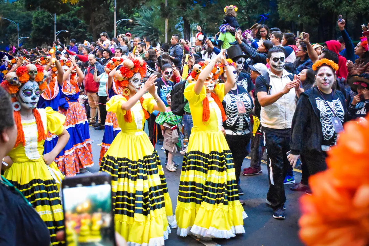 Un contingente de catrinas con vestidos amarillos de holanes baila en la calle rodeado de público