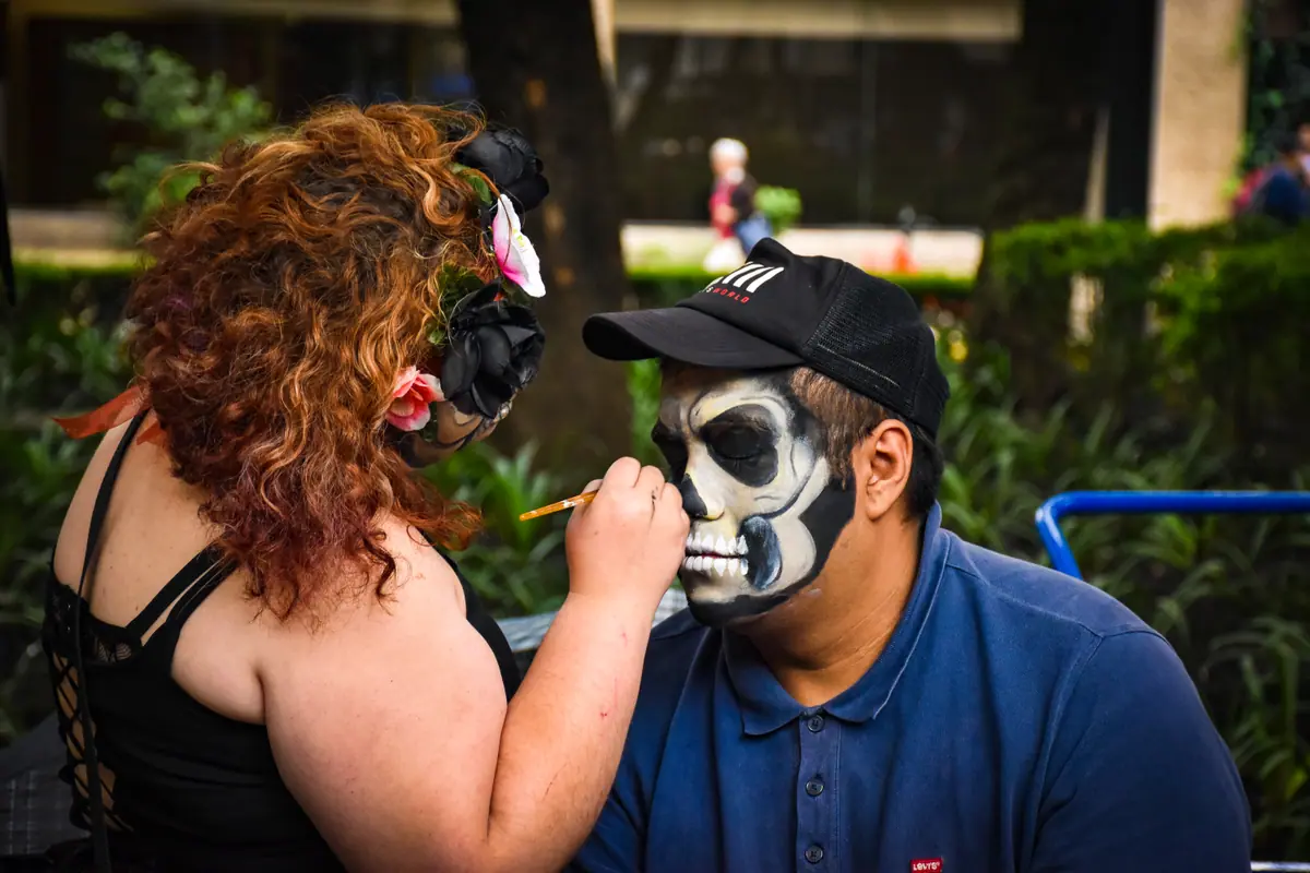 Una maquillista pinta de catrina el rostro de un asistente en la Mega Procesión de Catrinas de 2019