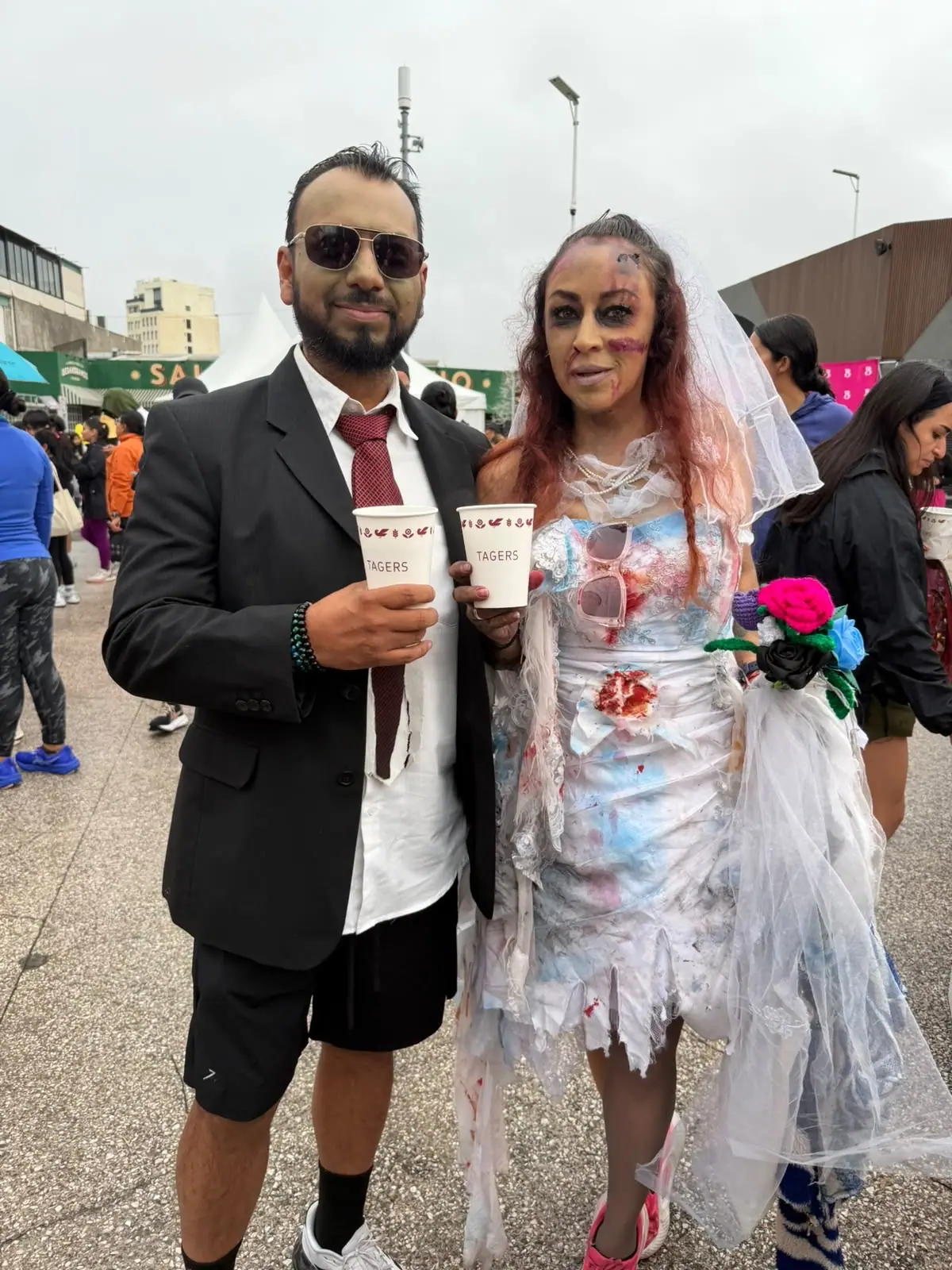 Pareja disfrazada de novios zombis con vasos de café de Tagers