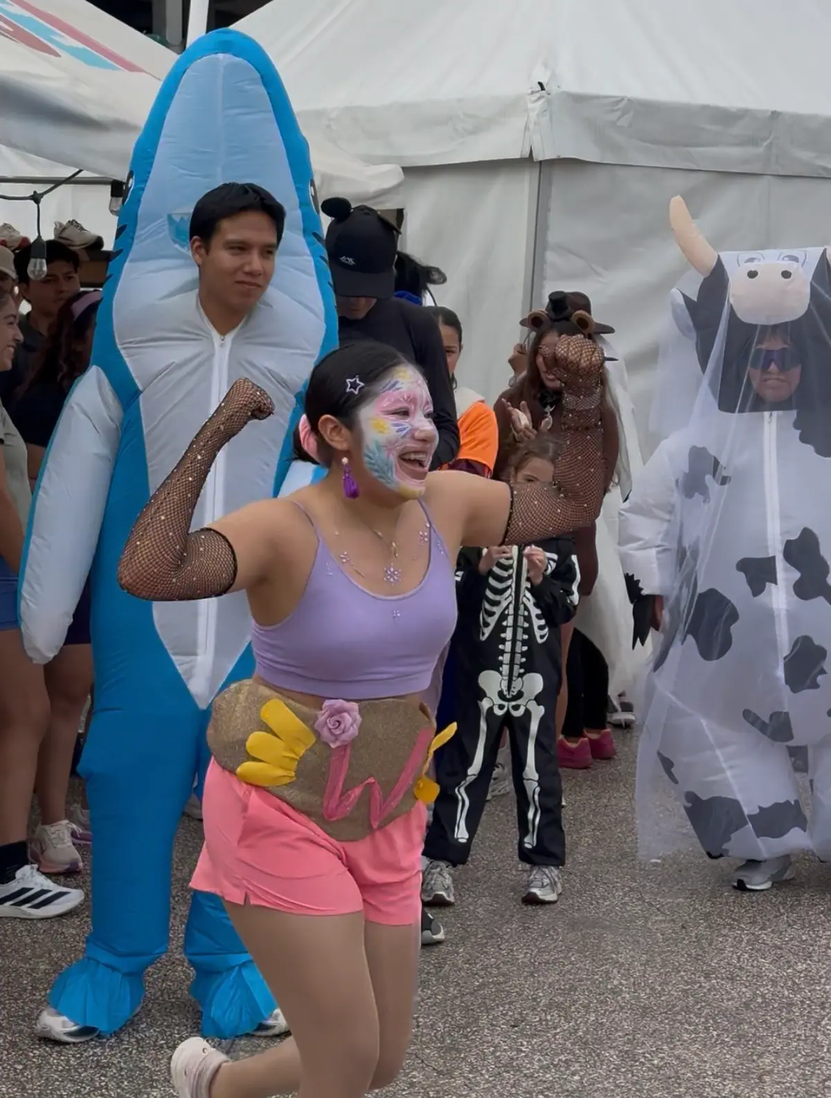 Participante con maquillaje de fantasía baila junto a un disfraz de tiburón