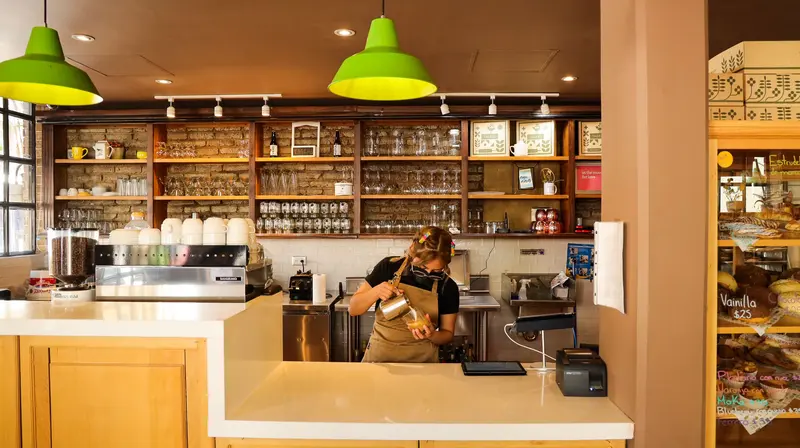 Barista preparando café en la barra de Tagers 5 Sur, bajo lámparas verdes