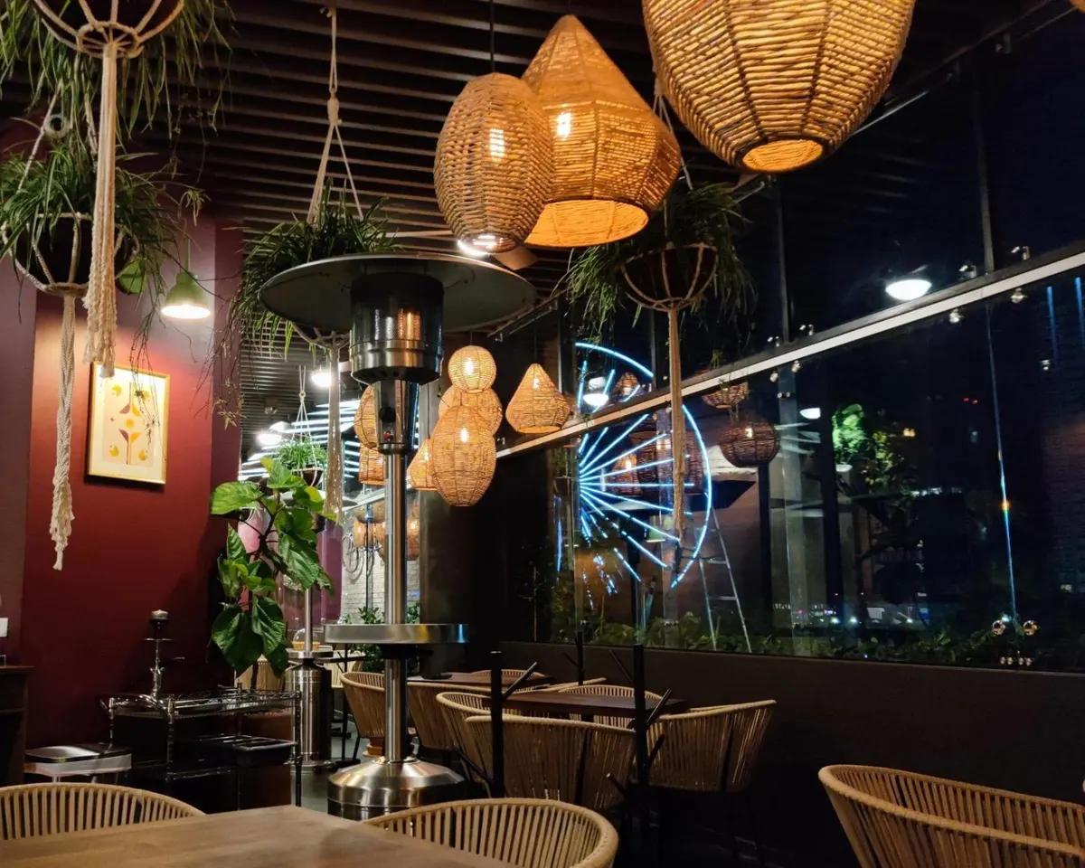 Terraza de Tagers Paseo Angelópolis de noche, con lámparas tejidas encendidas y la Estrella de Puebla iluminada al fondo