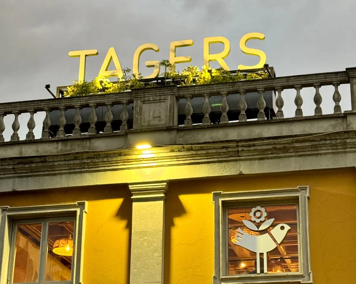 La casona amarilla de Tagers San Ángel al atardecer, con el letrero encendido sobre la balaustrada, en Av. de la Paz 40